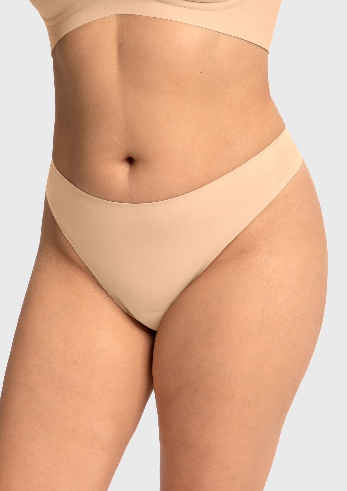 Model wearing the beige HSIA SmoothFit seamless thong, a perfect nude shade with built-in camel toe prevention for yoga pants.